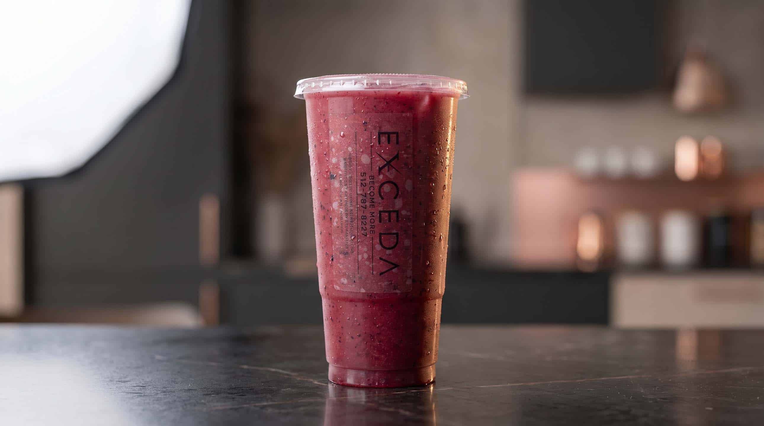 A deep red Exceda drink in a branded cup on a dark stone counter.