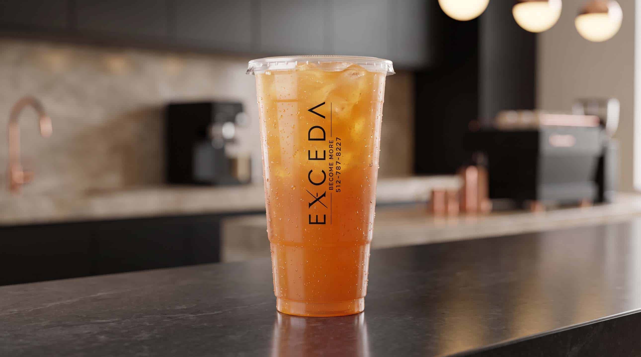An amber Exceda iced tea over ice in a branded cup on a dark counter.