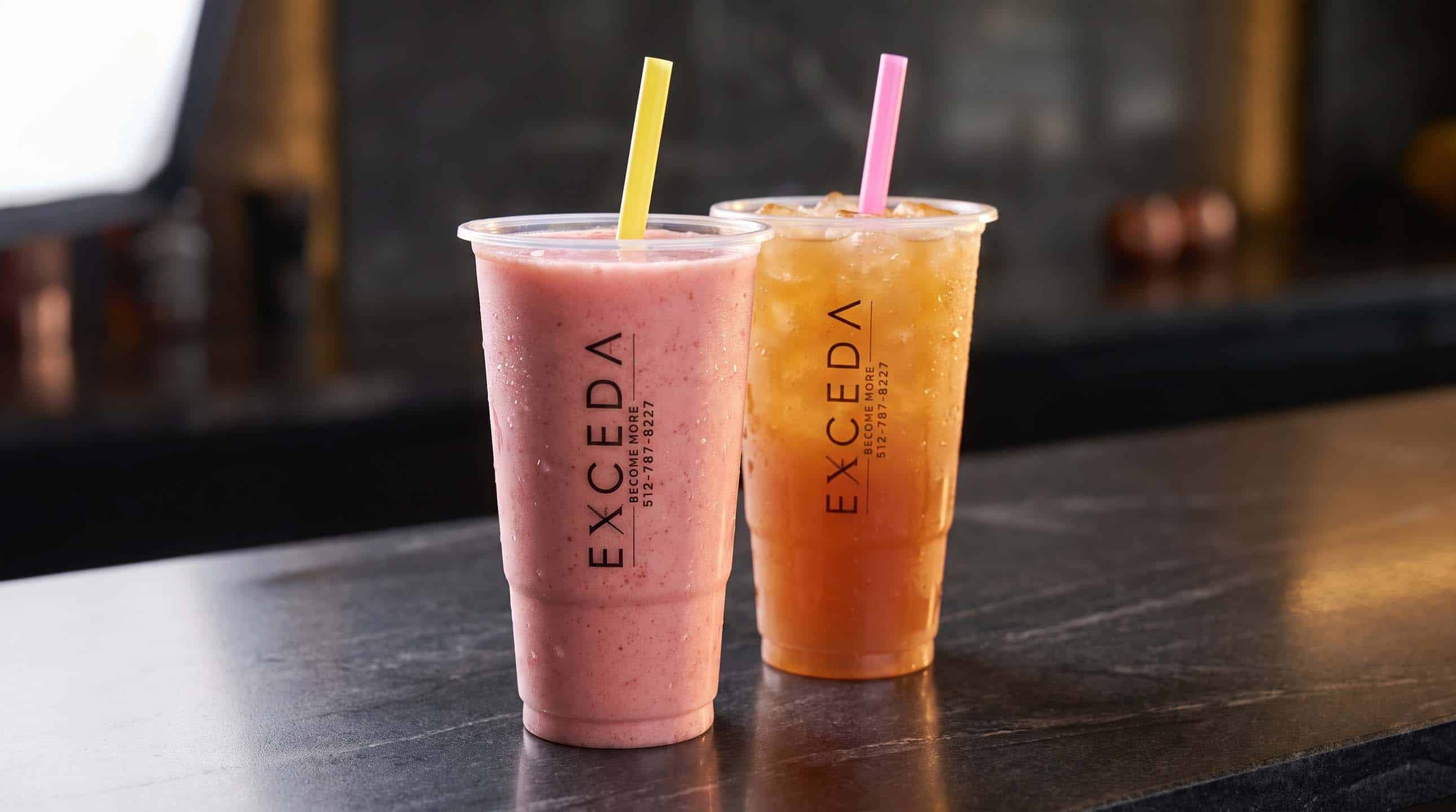 Two Exceda drinks side by side in branded cups, one pink and one orange.